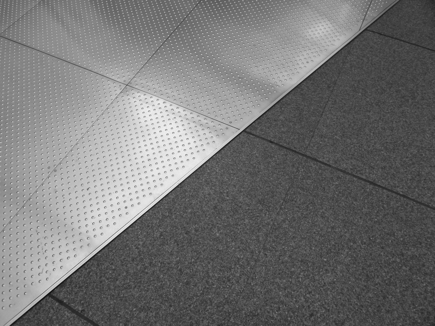 Modern flooring with silver metal and grey tiles meeting diagonally.